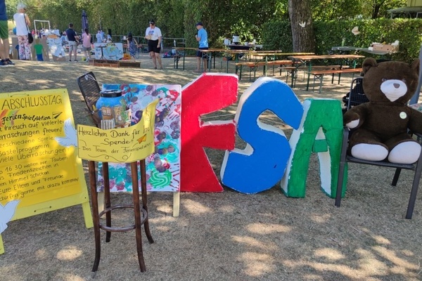 Plakat Abschluss Ferienspielaktion, Spendenk&auml;ssle, aufgestellte Buchstaben FSA und Teddyb&auml;r auf einem Stuhl