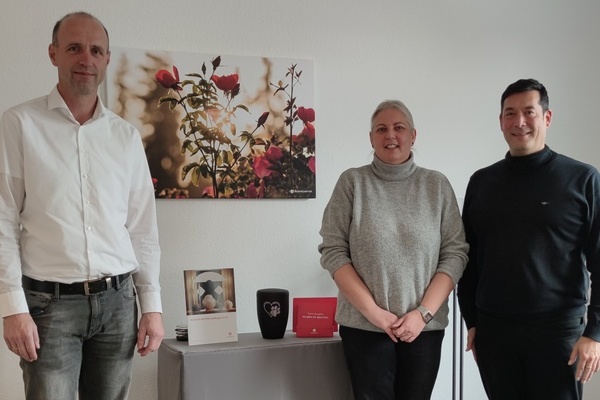 Herr Thorsten Hermes (Abteilungsleiter Filialmanagement), Frau Sandra Gall (Gebietsleiterin Baden-W&uuml;rttemberg), B&uuml;rgermeister Markus Hollemann stehend vor einem Rosen-Bild und einer Urne in der Mitte