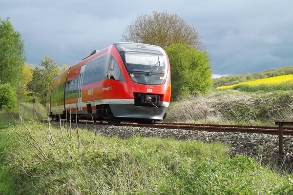 Roter Nahverkehrszug der Deutschen Bahn fährt durch grüne Landschaft