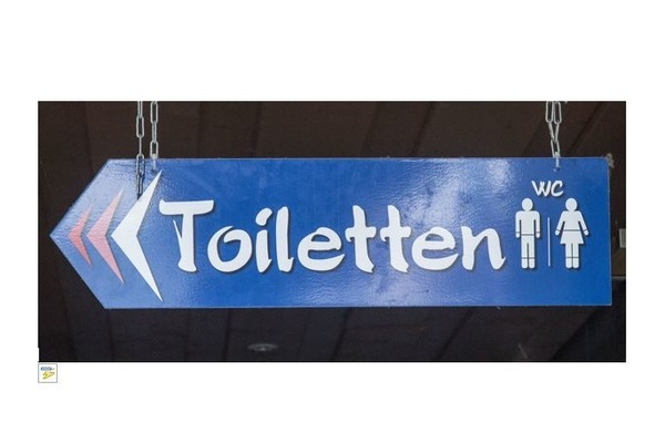 Blaues Hinweisschild in Pfeilform nach links mit weißer Aufschrift Toiletten/WC und Zeichnung Mann/Frau