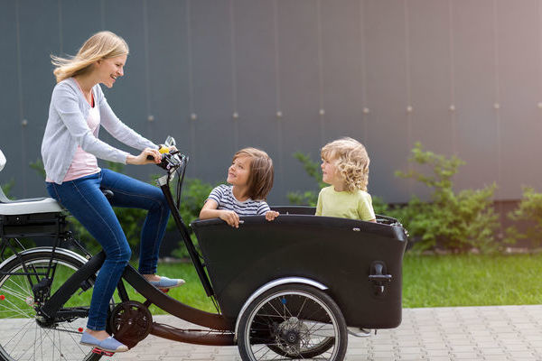 Eine Frau fhrt auf einem Lastenrad. Im Lastenkorb sitzen zwei Kinder