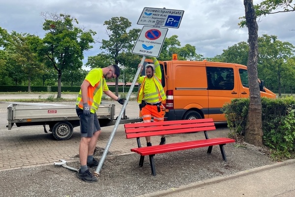 Stefan Schill (links) und Matthias Nübling vom Bauhof errichten die Beschilderung der neuen Bring- und Abholzone am MACH BLAU - mit Bänkle für Wartende. Foto: Katharina Schrader, Gemeinde Denzlingen