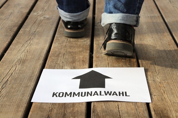 Schild mit schwarzer Schrift auf wei&szlig;em Grund. F&uuml;&szlig;e mit Schuhen.
