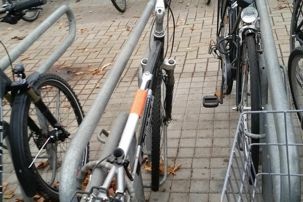 Mehrere abgestellt Fahrräder, ein Fahrrad mit rotem Aufkleber auf der Stange eines silbernen Herrenfahrrads Mehrere abgestellt Fahrräder, ein Fahrrad mit rotem Aufkleber auf der Stange eines silbernen Herrenfahrrads