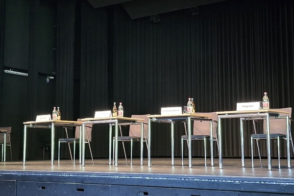Auf der Bühne stehen ein Rednerpult und vier Tische mit Namensschildern mit Stühlen für die vier Bewerber Auf der Bühne stehen ein Rednerpult und vier Tische mit Namensschildern mit Stühlen für die vier Bewerber