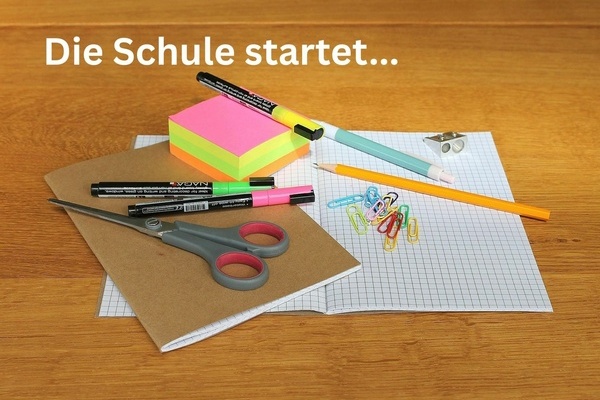 Die Schule startet ... Schulutensilien auf einem Tisch, weiße Schrift auf hölzernem Untergrund